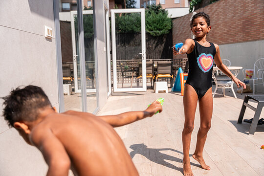 Hispanic family kids playing with water guns outdoors