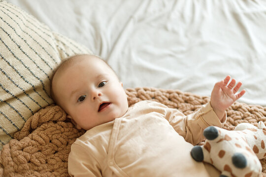 Cute happy  little baby lying on knitted blanket with sweet plush toy. Bedtime. Adorable infant portrait on bedding with space for text. Childhood and childcare.