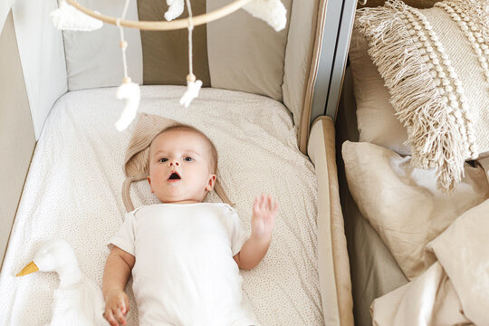 Adorable baby lying in crib with cute little toy and comforter. Time for sleep. Sweet infant portrait in boho bassinet top view. Childhood