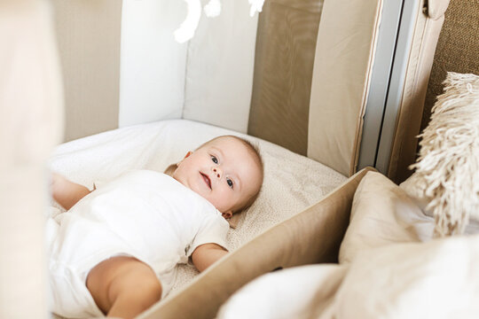 Adorable baby lying in crib with cute little toy and comforter. Time for sleep. Sweet infant portrait in boho bassinet top view. Childhood