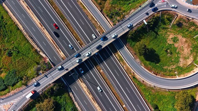 Aerial highway interchange with roundabout and overpass traffic. Drone top view of highway overpass, roundabout ramps, cars, lane markings, and green roadside areas.