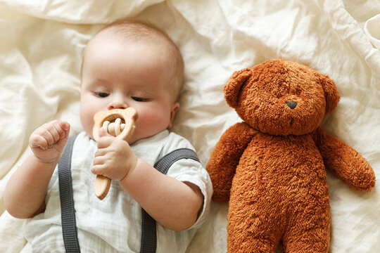 Adorable baby with cute teddy toy and teether lying on bed, top view. Time for sleep. Sweet infant portrait on soft bedding in morning light. Childhood