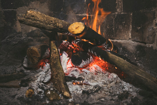 Burning firewood logs in rustic fireplace with glowing embers