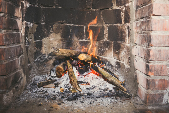 Burning firewood in brick fireplace with embers and ash