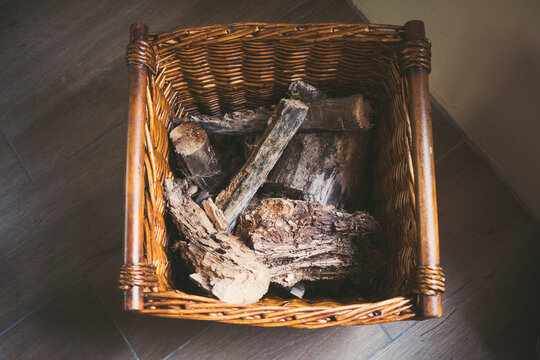 Rustic wicker basket filled with firewood on dark floor