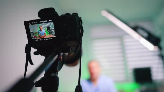 Side View Of Camera Filming Doctor In Clinic. Side view of camera and tripod filming doctor in clinic room with LED light and green background.