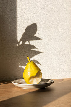 Minimal still life of bitten pear on plate in sunlight