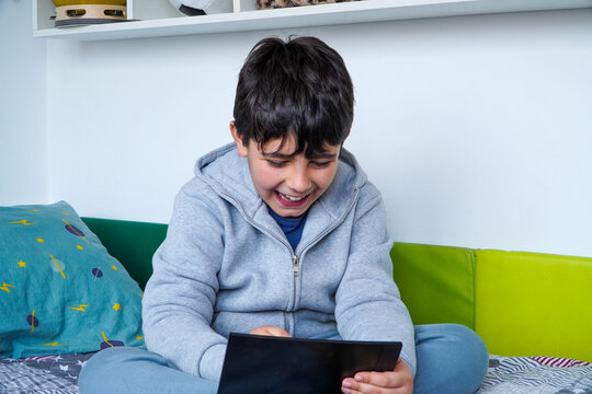 Happy gen alpha teen boy using tablet in bedroom at home