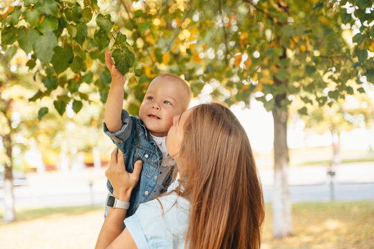 Mother holding son in park reaching for autumn leaves