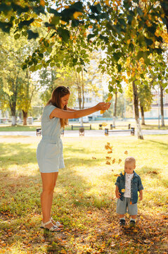 Mother and son playing with falling autumn leaves in park