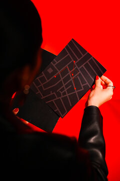 Person holds a dark, patterned map against a vibrant red backdrop