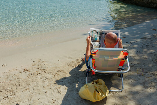 rear view of a Man Reading Newspaper in Beach Chair on Sunny Tropical Shore