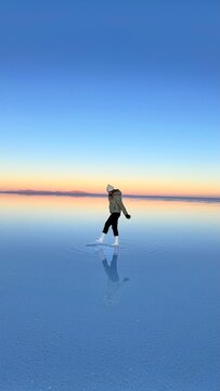 Woman reflected in shallow water at Salar de Uyuni at sunset, Bolivia