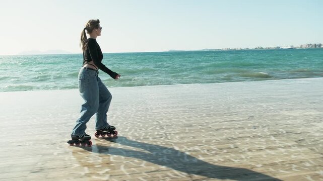 Woman roller skating along shallow beach water near sea, filmed with stabilizer in smooth parallel tracking shot. Bright sunlight, reflections on sand and active summer lifestyle concept.