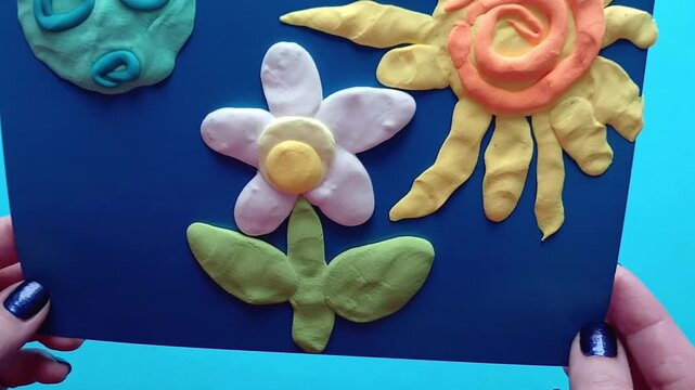 Raising and moving the drawing away from the camera, a colorful floral design made of modeling clay.
