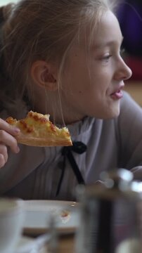 A cute girl eats pizza with her hands in a cafe. A hungry child munches on fast food. A snack at a cafe. High quality FullHD footage