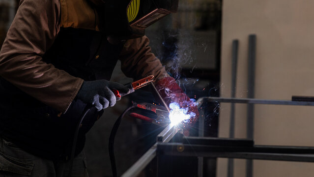 Welder works on metal frame in workshop during evening hours with sparks flying