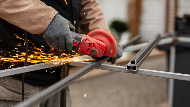 Metal worker uses a tool to cut steel while sparks fly at a construction site in the afternoon