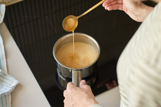 Person lifts thick sauce with spoon above saucepan on cooktop. Concept of home cooking