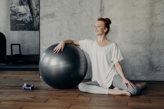 Fitness woman sitting on floor with exercise ball after workout in gym studio