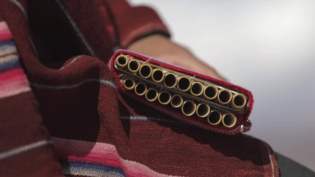 A hand holds a zampo&ntilde;a, dressed in a vibrant poncho featuring shades of red.