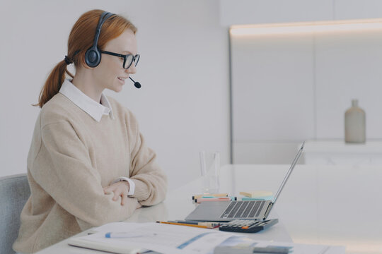 Female customer service agent wearing headset working on laptop in bright office