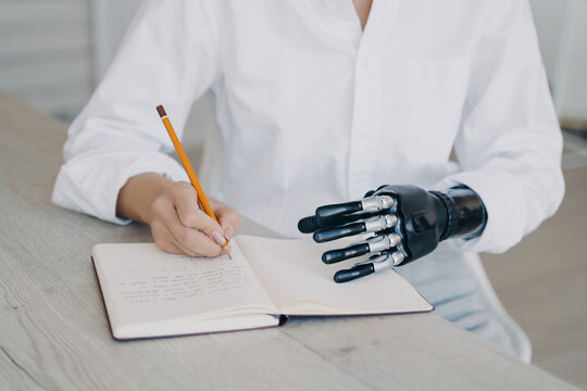Person with prosthetic hand writing in notebook at table indoors