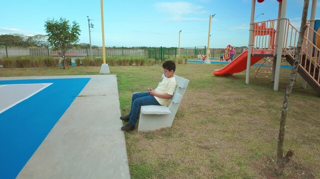 Boy using a smartphone sitting alone on a park bench