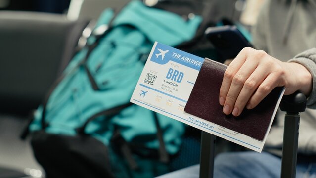 Close up of travel documents and phone used by man in crowded airport during international holidays season. Tourists holding passport and boarding plane ticket, going home, camera A