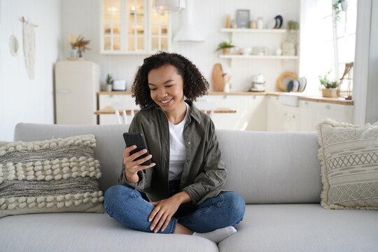 Young black woman using smartphone on sofa in bright modern living room at home