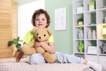 Smiling little boy hugging plush toy bear on pouf at home. Space for text © New Africa