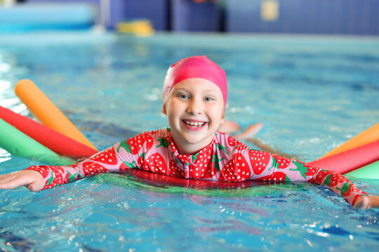 Cute little girl swimming with water noodles during lesson in pool
