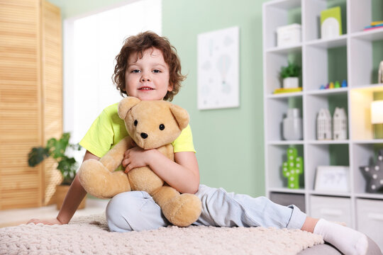Smiling little boy hugging plush toy bear on pouf at home. Space for text