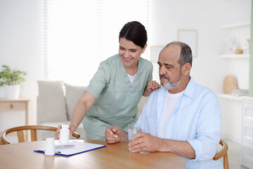 Obraz premium Smiling care worker working with senior man at wooden table at nursing home