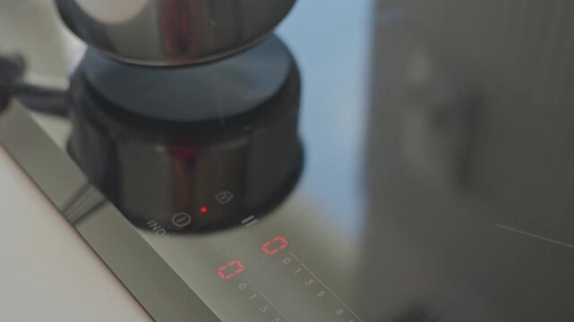 Hand touches control panel on induction cooktop before placing small saucepan. Concept of kitchen appliance use and meal preparation