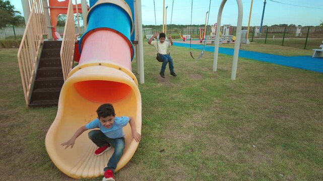Happy children playing on a playground slide and swing set