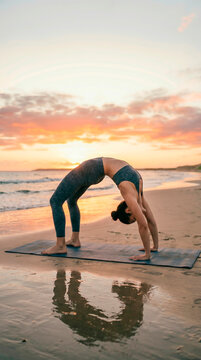 Woman performing wheel pose yoga on beach, vertical format, flexibility and strength concept