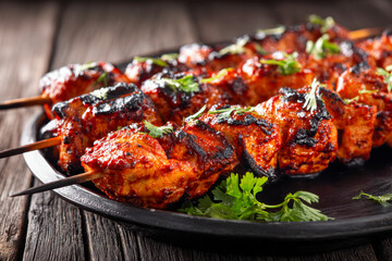 Fototapeta premium Grilled marinated chicken skewers with spices garnished with fresh herbs served on a black plate over rustic wooden table background