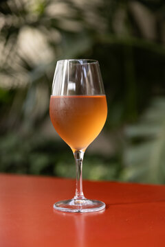 Glass of orange wine on bright red table with plants in the background.
