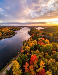 Obraz premium Aerial view of a winding river surrounded by vibrant autumn foliage under a dramatic sunset sky. A path follows the riverbank