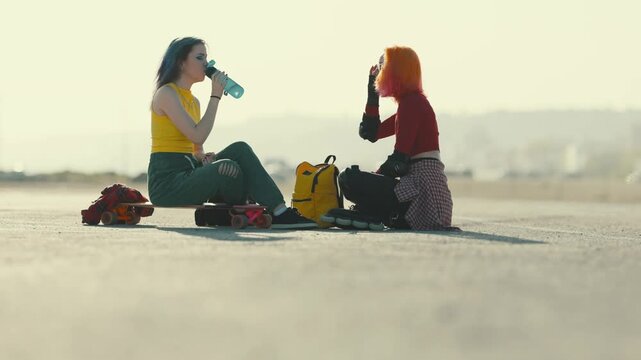 Teenage girls resting and drinking water after roller skating