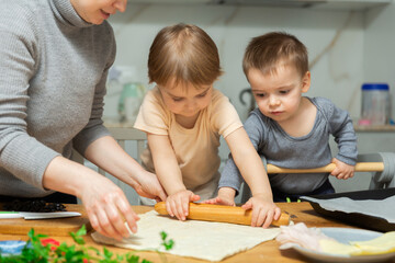 Obraz premium Toddler children help mom cook pizza. Family activity for development of fine motor skills. Child lays out pieces of bacon on pizza base dough.
