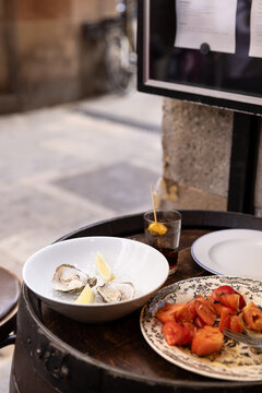 oysters with lemon, tomato salad, glass of vermouth, outdoor dining in spain on barrel tabletop with street in the background