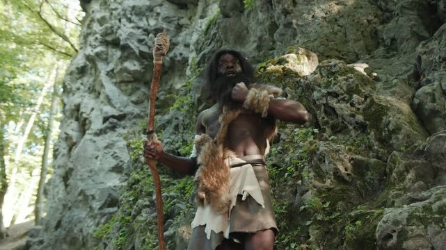 A Primitive Warrior stands assertively in a vast Natural Landscape, gripping a Staff