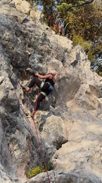 LOW ANGLE VIEW: Agile young woman lead climbing a pale limestone route outdoors in summer. Skilful female climber moves dynamically over an overhang, showing strength, agility, focus and technique.