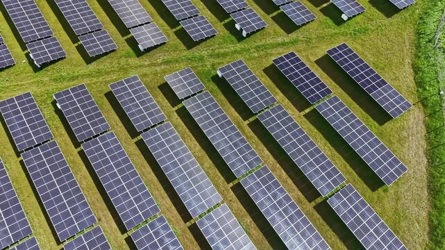 Rows of solar panels cover a wide area of land, reflecting sunlight. This setup highlights the use of renewable energy technology to generate power in an open field.