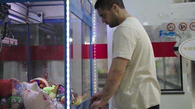 Close-up of man playing claw crane machine to catch a toy