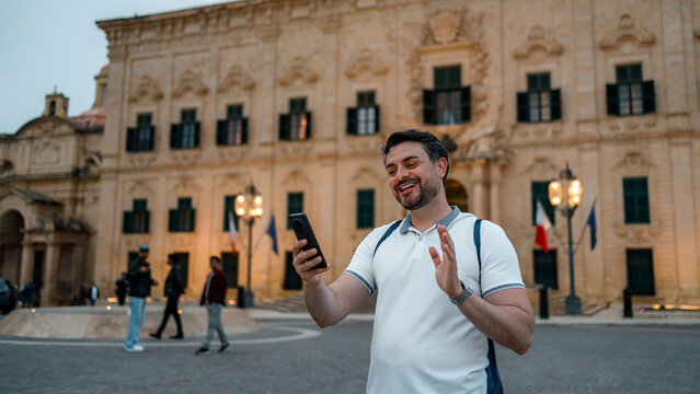 Man using smartphone on a street in Malta during evening time with historic building in background
