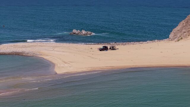 Aerial view shows an SUV with a teardrop camper trailer parked on the beach at Punta Final in Baja California, Mexico.