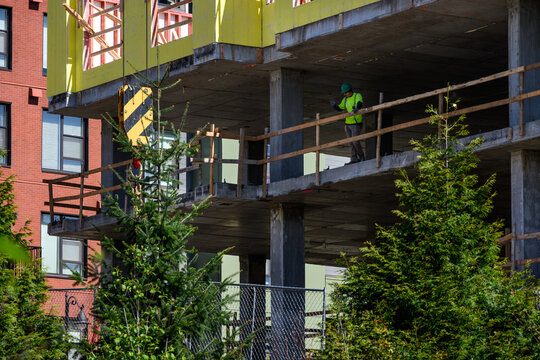 Construction worker standing at railing on concrete floor of new residential high rise building, new real estate development, wood framing and external sheathing
